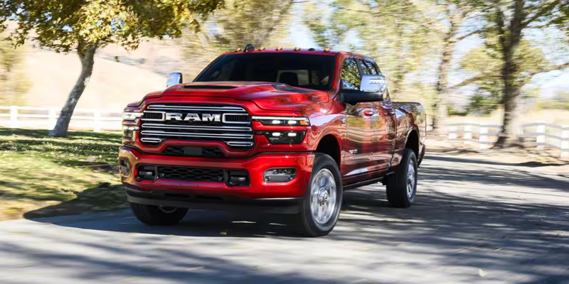 A red RAM 2500 truck driving down a tree-lined road, showcasing its powerful and bold design.