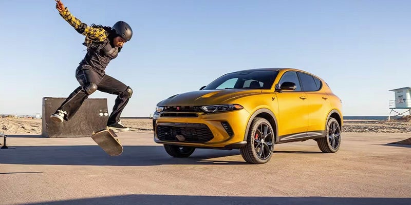 front left view of a yellow 2024 dodge hornet with a person doing skateboard trick in the foreground