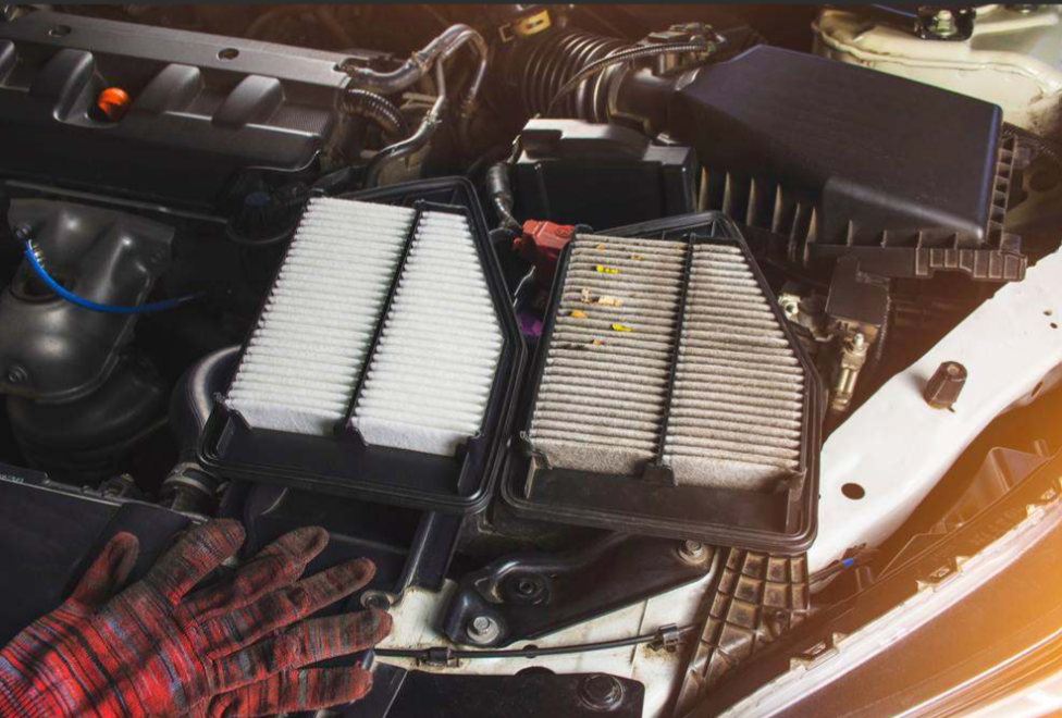 Vehicle air filter replacement showing new and dirty filters inside an engine compartment.