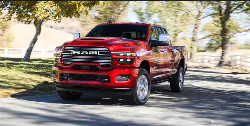 Red RAM pickup truck driving on a tree-lined road in a rural setting.